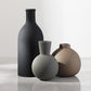 Three ceramic vases of different shapes and colors on a reflective surface with a light gray background