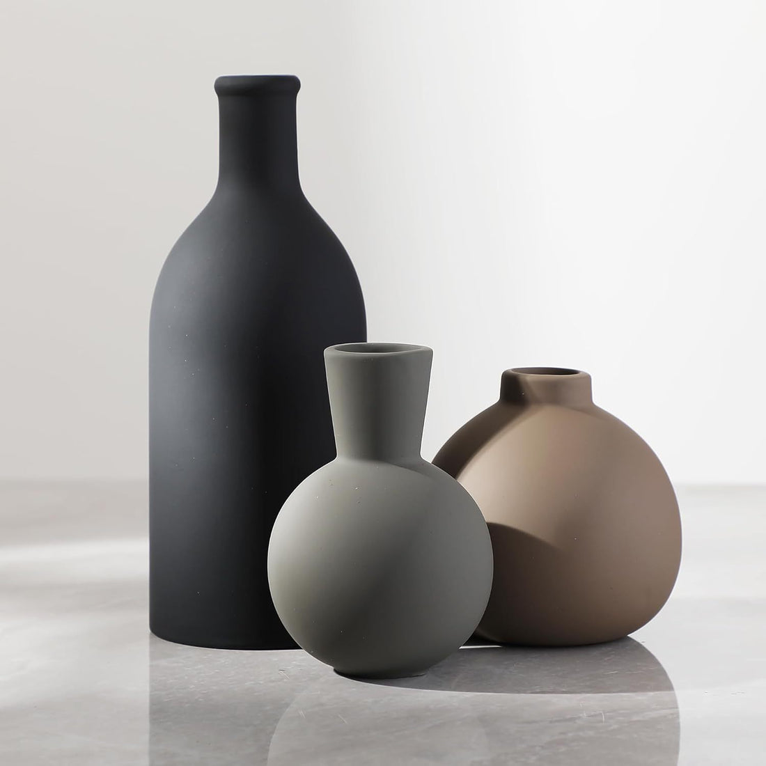 Three ceramic vases of different shapes and colors on a reflective surface with a light gray background