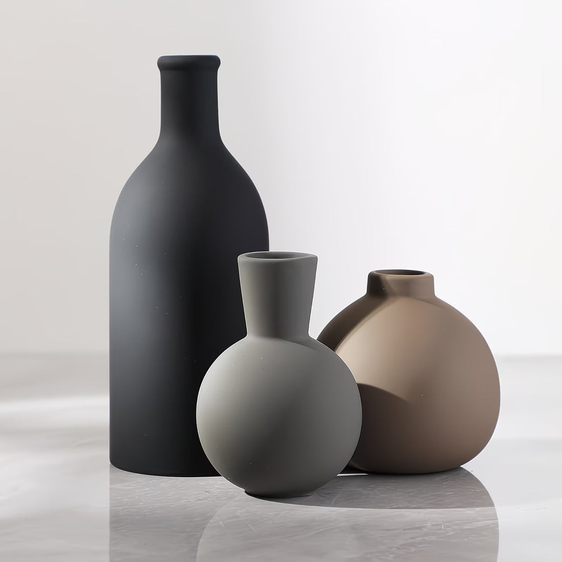 Three vases of different shapes and colors on a reflective surface with a light gray background