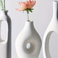 White ceramic vases with circular designs and flowers on a light gray background