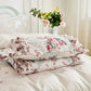 Floral patterned pillows on a bed with a vase of flowers in the background