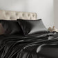 Black satin pillowcases on a bed with a neutral headboard.