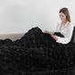 Woman reading a book under a large black blanket on a couch.
