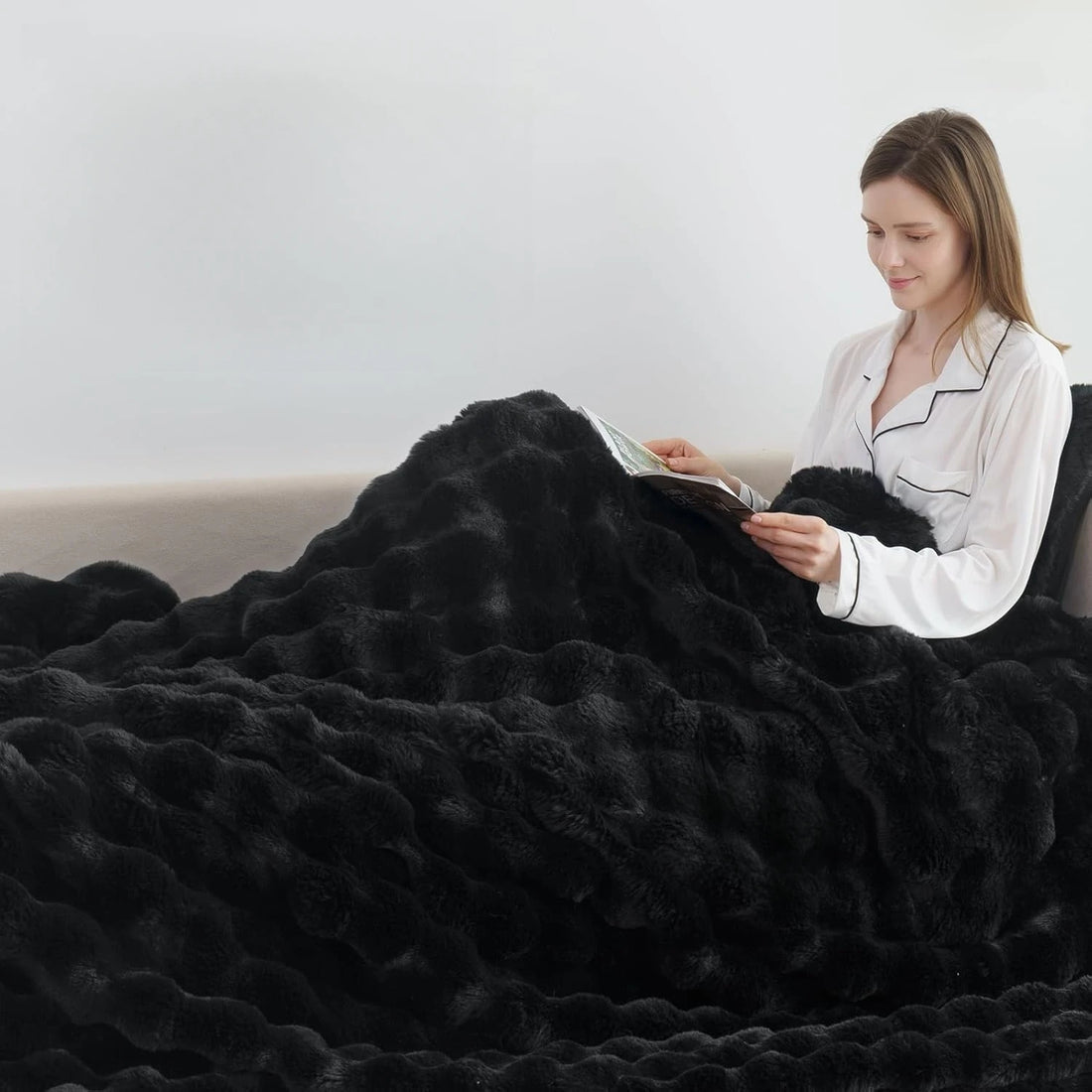 Woman reading a book under a large black blanket on a couch.