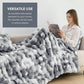 Woman reading a book under a large gray blanket in a cozy living room.