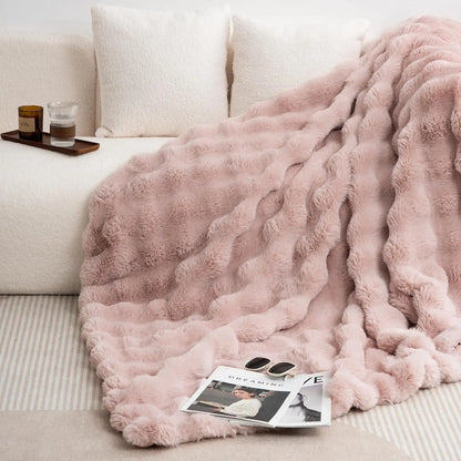 Pink fluffy blanket draped over a sofa with a magazine and sunglasses on it.
