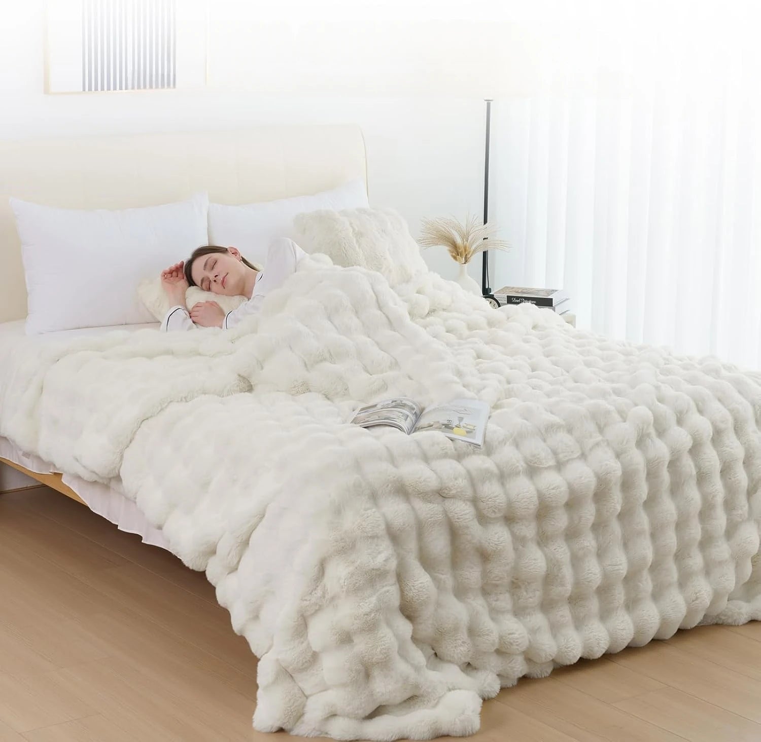 Person lying in bed under a fluffy white comforter in a bright bedroom.