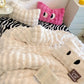 Fluffy white blanket with black accents on a bed with zebra-patterned bedding and a pink pillow.