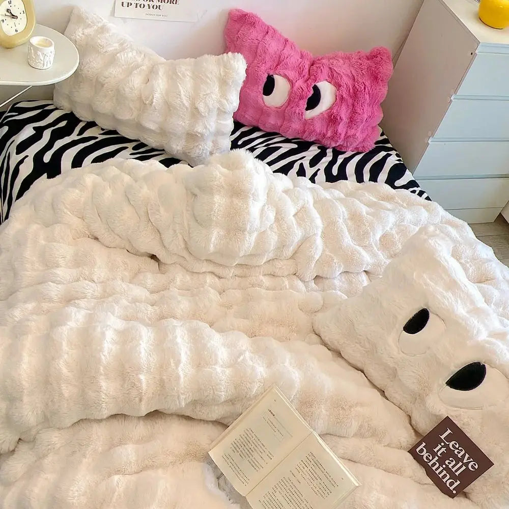 Fluffy white blanket with black accents on a bed with zebra-patterned bedding and a pink pillow.