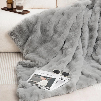 Gray fluffy blanket draped over a couch with a magazine and sunglasses on top
