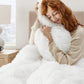 Woman hugging a fluffy white pillow in a cozy room.