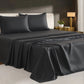 Black bedspread on a bed in a bedroom setting with a lamp and plant in the background.