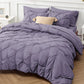 Purple textured comforter on a bed with pillows and a side table in the background.