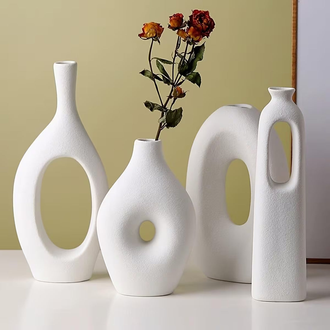 Set of four white ceramic vases with unique designs on a light surface.