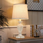 Decorative table lamp on a wooden surface with books and a plant in the background