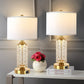 Two table lamps with decorative bases on a surface with books and flowers.