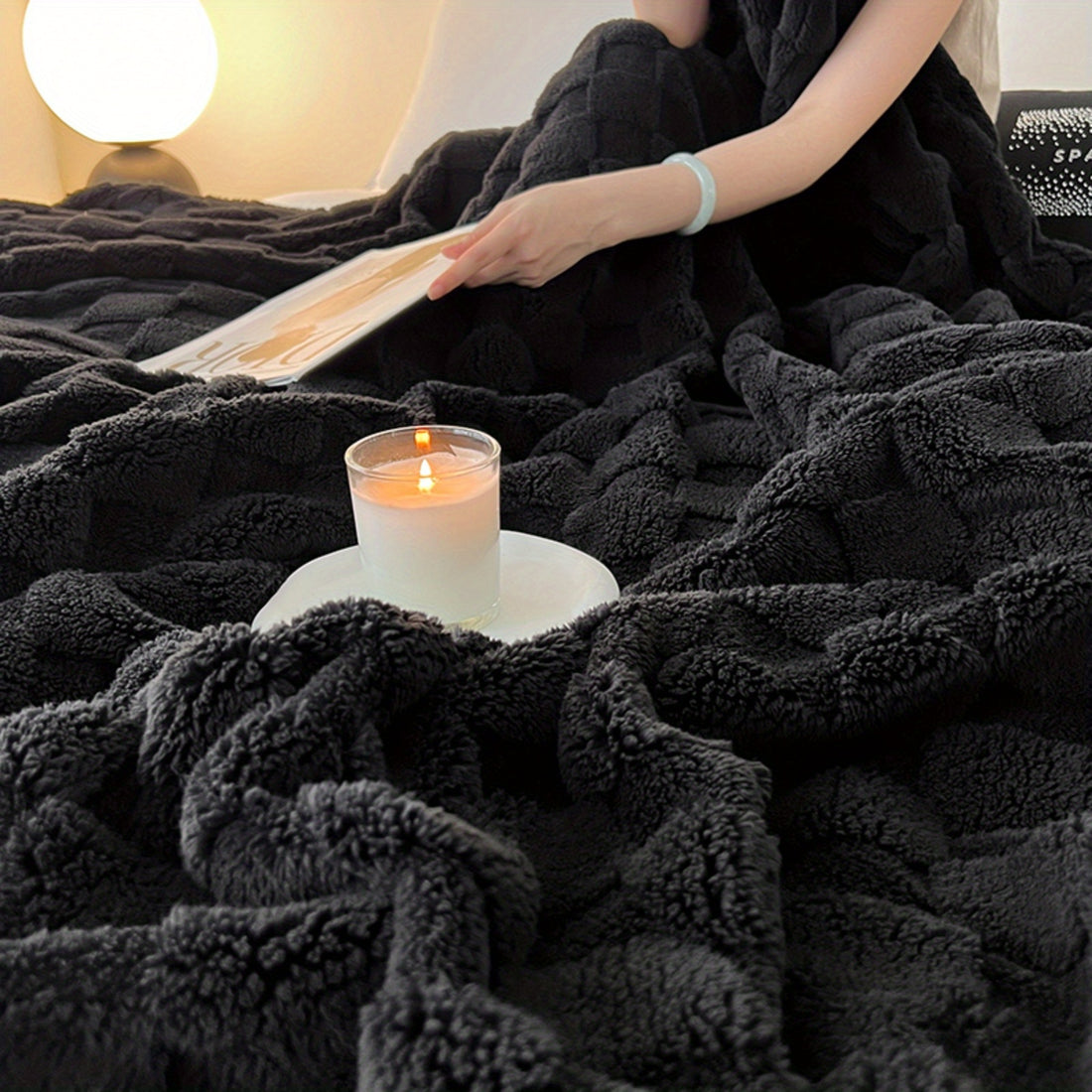 Person reading a book on a black blanket with a lit candle beside them.