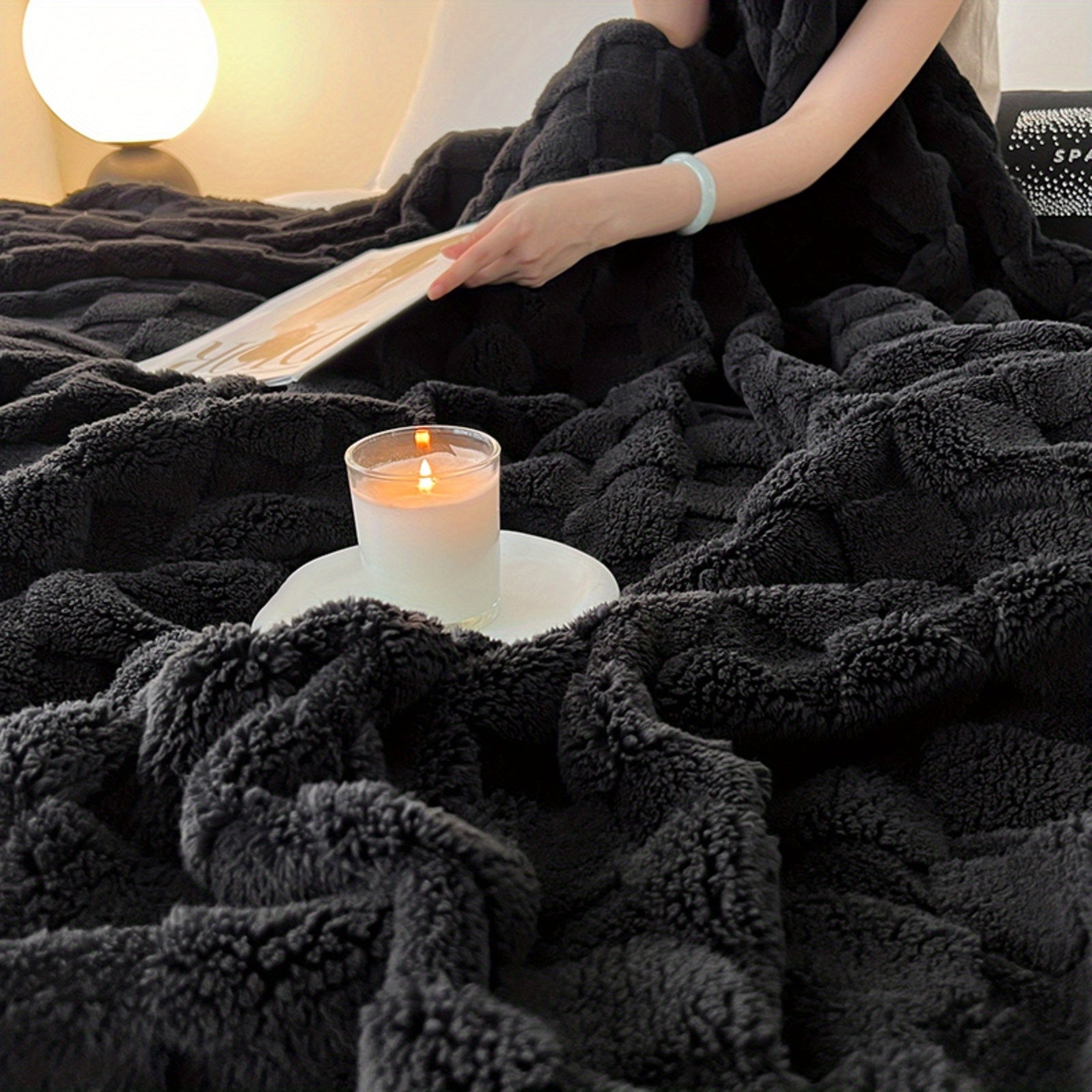 Person reading a book on a black blanket with a lit candle beside them.