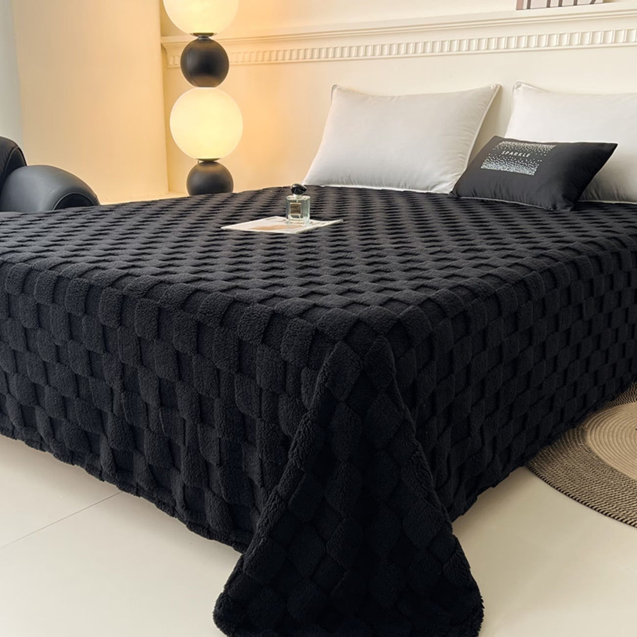 Black textured blanket on a bed in a bedroom setting with lamps and pillows.
