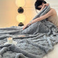Person wrapped in a soft gray blanket in a cozy room with a lamp and candle.