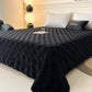 Black textured blanket on a bed in a bedroom setting with lamps and pillows.