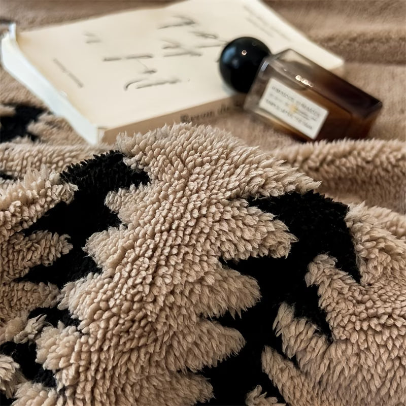 Close-up of a textured beige blanket with black patterns, a book, and a bottle on a surface.