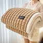 Folded beige blanket with 'HOME' label held by a person against a white curtain background