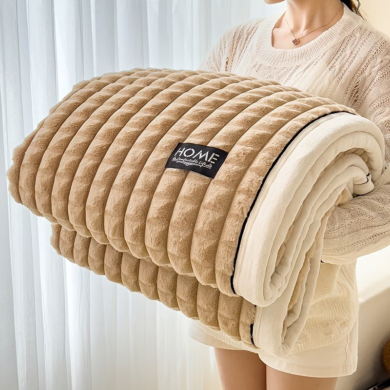 Folded beige blanket with 'HOME' label held by a person against a white curtain background