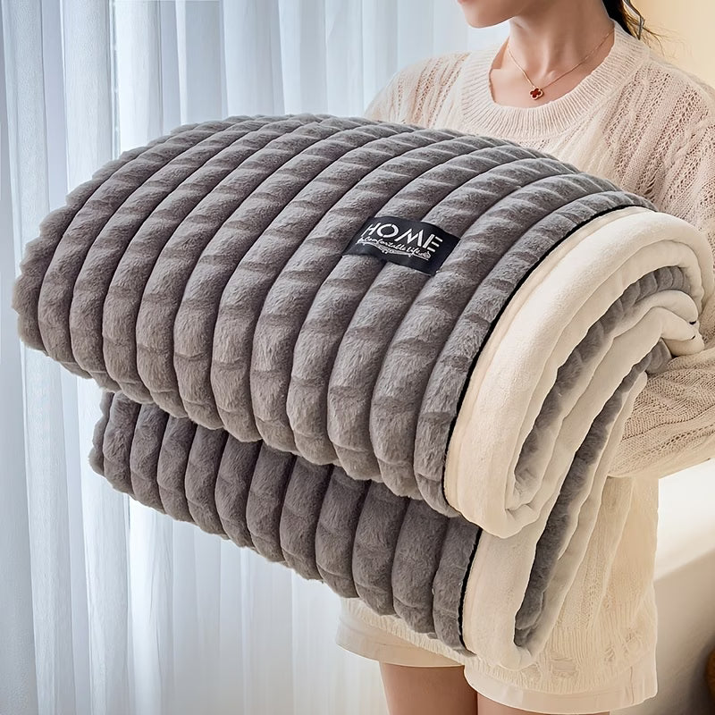 Folded gray and beige blanket with a brand label held by a person against a light curtain background