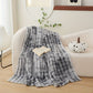 Gray tie-dye blanket draped over a white couch with a book and decorative pumpkin on a wooden floor.