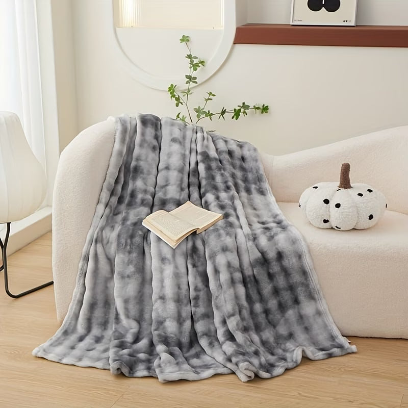 Gray tie-dye blanket draped over a white couch with a book and decorative pumpkin on a wooden floor.