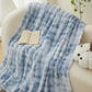 Blue patterned blanket draped over a couch with an open book and plush toy.