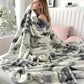 Woman wrapped in a gray and white patterned blanket on a bed with a cup of tea.