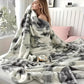 Woman wrapped in a gray and white patterned blanket on a bed with a cup of tea.