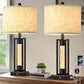 Two table lamps with fabric shades on a wooden surface, with a smartphone and small plant in the background.