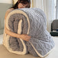 Person holding a large gray and white textured blanket in a bedroom setting.
